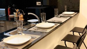 A long kitchen counter with a sink, a kettle, and a glass of water. There are plates, cutlery, and a chair. - Santo Domingo Apartment with Rooftop Pool with Ocean & City Views (Santo Domingo)