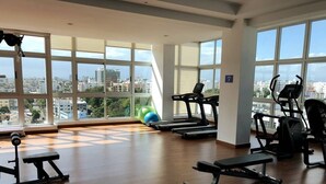 A gym with treadmills, a bench, and exercise balls, with large windows offering a city view. - Santo Domingo Apartment with Rooftop Pool with Ocean & City Views (Santo Domingo)