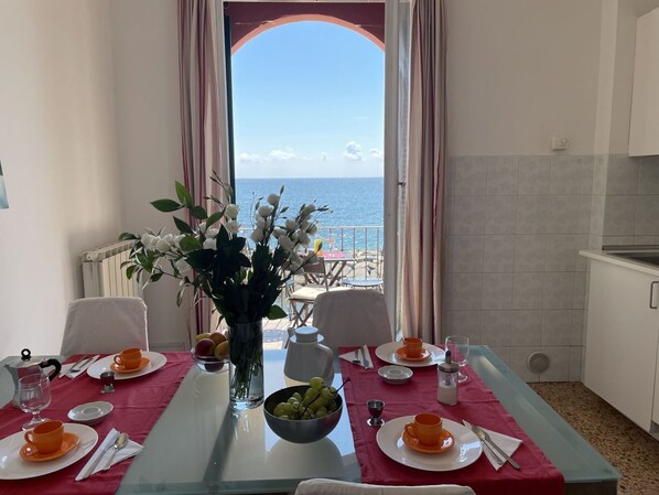 A dining area with a table set for two, a vase with flowers, and a view of the sea through an open archway. - Beautiful apartment for 5 guests with WIFI, TV, balcony and pets allowed (Imperia)