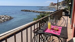 A balcony with a table set for dining, overlooking a rocky coastline and the sea. - Beautiful apartment for 5 guests with WIFI, TV, balcony and pets allowed (Imperia)