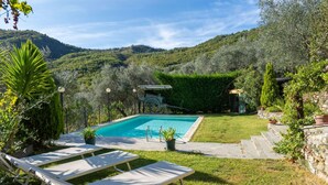 A pool with lounge chairs, surrounded by a well-maintained garden and a view of a hilly landscape. - Beautiful private villa with A/C, private pool, WIFI, TV, patio, pets allowed and panoramic view (Borgomaro)