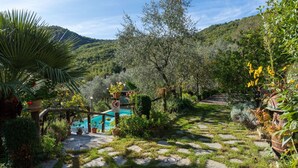 A garden with a stone pathway leading to a pool, surrounded by lush greenery and trees. - Beautiful private villa with A/C, private pool, WIFI, TV, patio, pets allowed and panoramic view (Borgomaro)