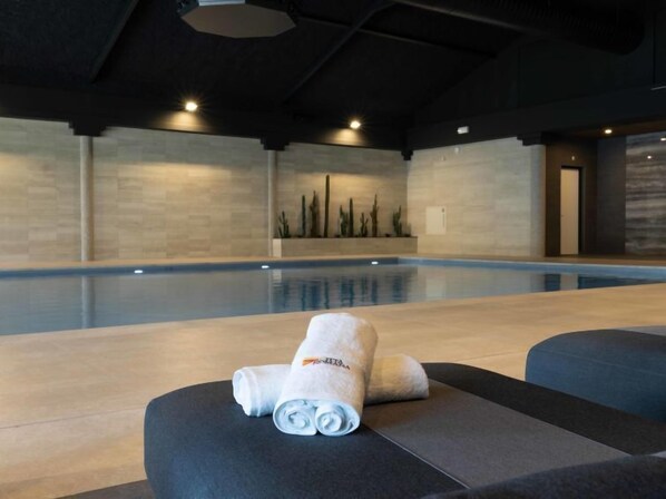 A modern indoor pool area with a large pool, dark ceiling, and minimalist decor.