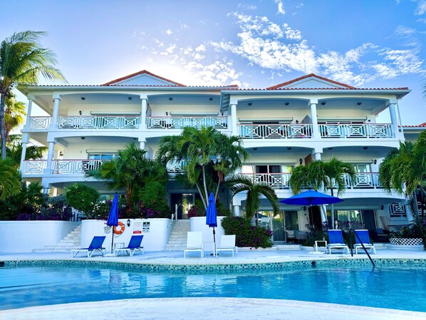 A multi-story hotel with a swimming pool, balconies, and lounge chairs.