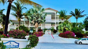 Un hotel con fachada blanca, varios balcones y exuberante jardinería tropical.
