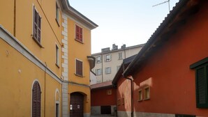 Una estrecha calle adoquinada entre edificios con fachadas amarillas y rojas, que presenta puertas arqueadas y ventanas con contraventanas.