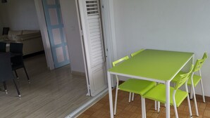 Een eethoek met een groene tafel en bijpassende stoelen, een witte deur en een beige bank op de achtergrond.
