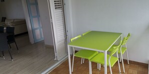 A dining area with a green table and matching chairs, a white door, and a beige sofa in the background. - Rent villa in Martinique (Le Vauclin)