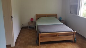 Een slaapkamer met een houten bed, een nachtkastje met een rode lamp en een raam met jaloezieën.