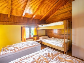 Una camera in stile baita con due letti a castello e un letto singolo, pareti in legno e una finestra con tende.
