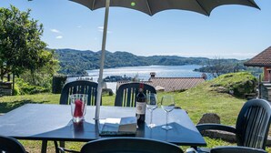 An outdoor table with a large umbrella, a bottle of wine, and glasses, overlooking a scenic lake and hills. - Beautiful private villa for 6 guests with WIFI, TV, patio and pets allowed (Pella)