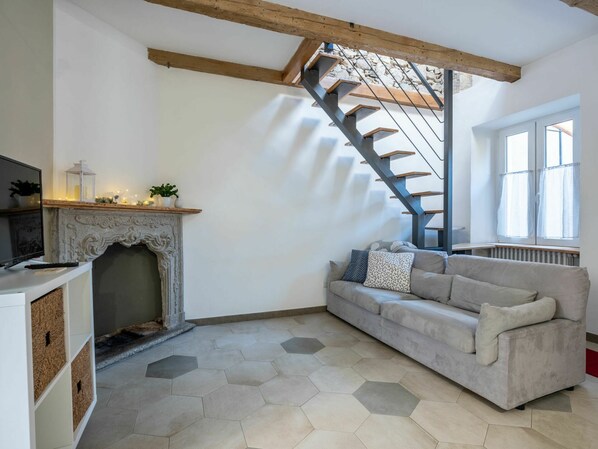 A living room with a fireplace, a sofa, a staircase, and a window.