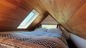 Quarto com teto inclinado, claraboia e cama com roupa de cama estampada.