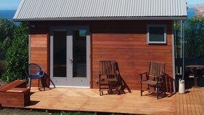 Uma cabana de madeira com telhado de metal, um deck com área de estar externa e vista para o oceano.