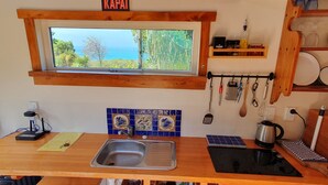 Uma cozinha com janela, pia, fogão e diversos utensílios pendurados na parede.