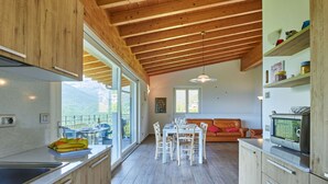 A modern kitchen with a dining area, wooden ceiling beams, and large windows offering a view of the outdoors. - Beautiful private villa for 8 guests with WIFI, TV, terrace and pets allowed (Peglio)