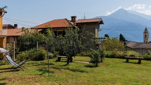 A house with a tiled roof, a small garden with a bench, and a mountain in the background.