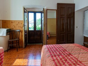 A room with a bed, a chair, a wooden door, and a view through the door.