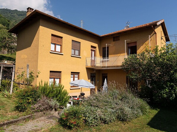 A two-story building with a balcony, a patio with outdoor seating, and a garden area.