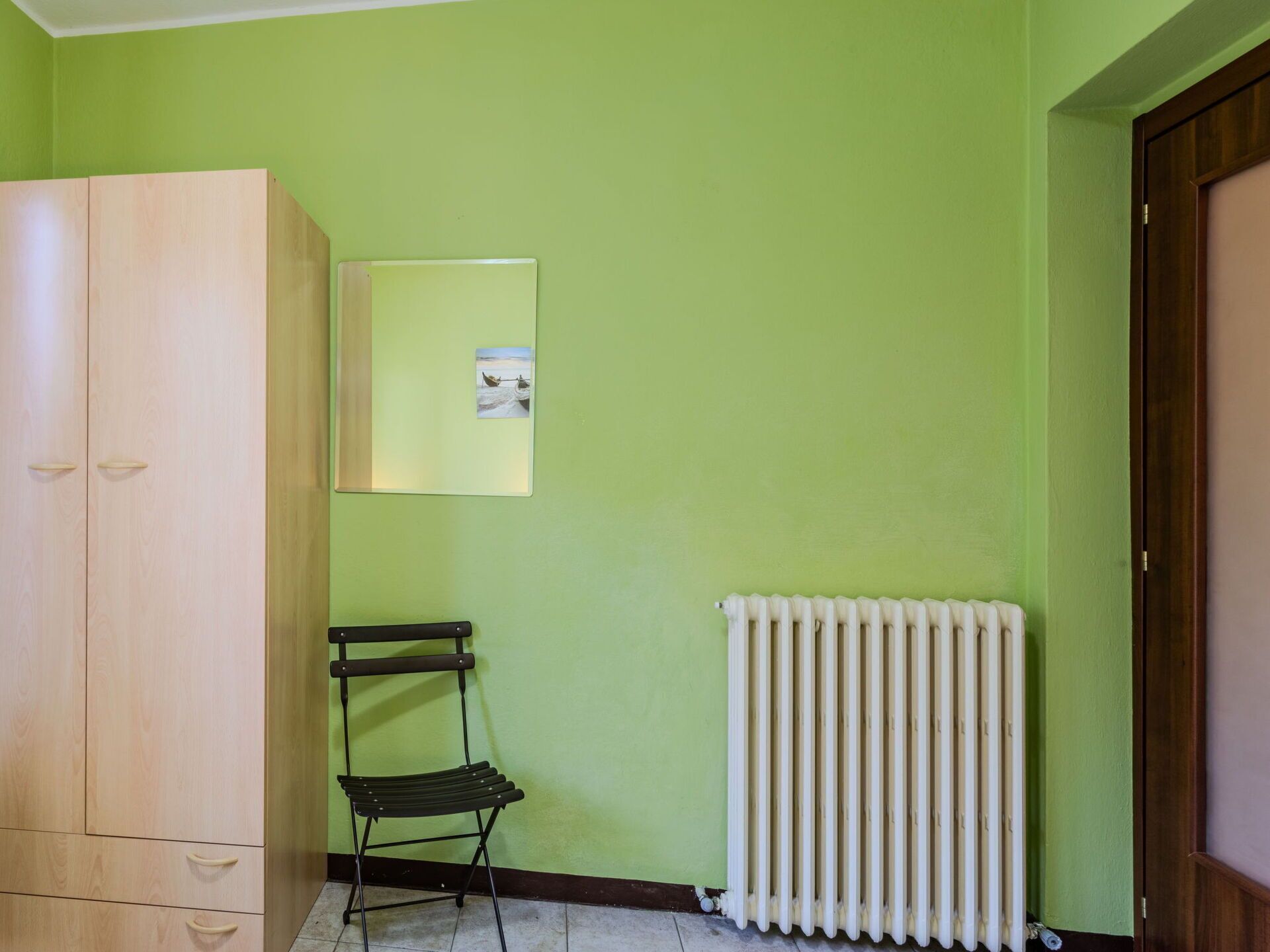 A room with a wooden wardrobe, a radiator, and a small chair.