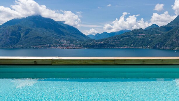 Ein Pool mit Holzterrasse, umgeben von Bergen und einem See.