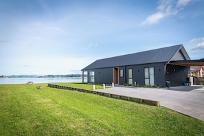 Une maison moderne avec un garage, une cour verdoyante et une vue sur un lac.