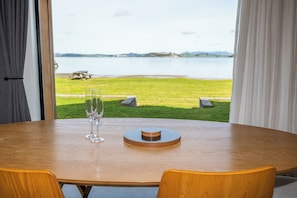 Une table Ă manger avec deux verres Ă vin et une pile de sous-verres, donnant sur une zone herbeuse avec un plan dâeau et des collines au loin.