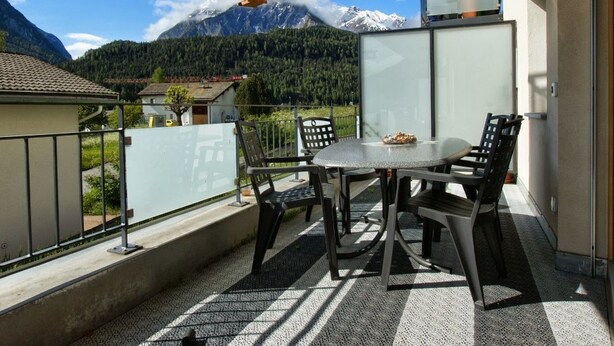 Un balcón con mesa y sillas, con vista a una montaña y su cima nevada.