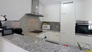 Una cocina moderna con gabinetes blancos, encimeras de granito, una campana extractora de acero inoxidable, un microondas y un horno.