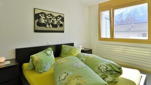 Un dormitorio con cama, mesita de noche, ventana con vistas y un cuadro colgado en la pared.