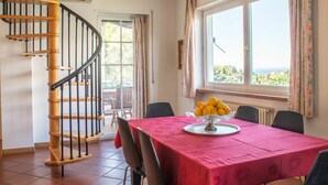 Un comedor con una mesa dispuesta para cuatro, una escalera de caracol y una ventana con vistas.
