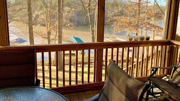 A wooden deck with a glass railing, a table, and two chairs. - Lake Front Home. 3 Large Living Spaces. Screened Porches. Pet Friendly. (Lavonia)