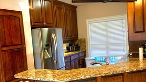A kitchen with wooden cabinets, a stainless steel refrigerator, a granite countertop, and a pendant light fixture. - Lake Front Home. 3 Large Living Spaces. Screened Porches. Pet Friendly. (Lavonia)