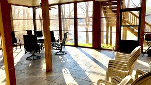 A covered outdoor seating area with chairs and tables, large windows, and a wooden staircase. - Lake Front Home. 3 Large Living Spaces. Screened Porches. Pet Friendly. (Lavonia)