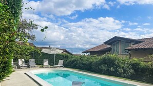 Une piscine rectangulaire dotée d’un toboggan intégré, entourée de chaises longues blanches et agrémentée d’un parasol.
