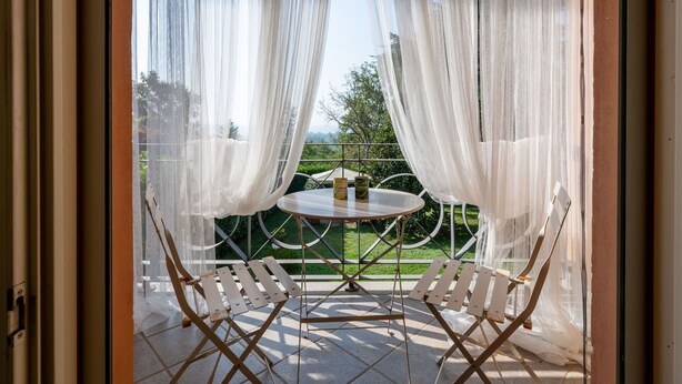 Un balcon agrémenté d’une table et de chaises, et orné de rideaux blancs et légers.