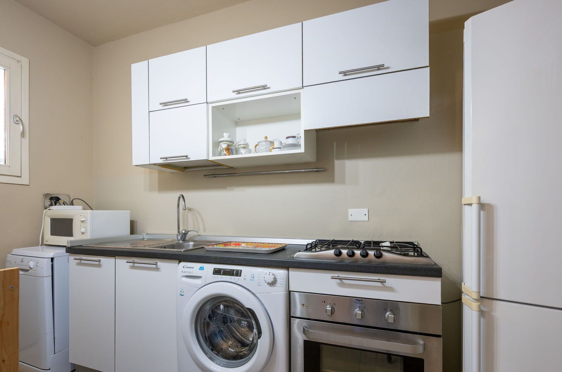 Cocina compacta con armarios blancos, microondas, lavadora, estufa y refrigerador.