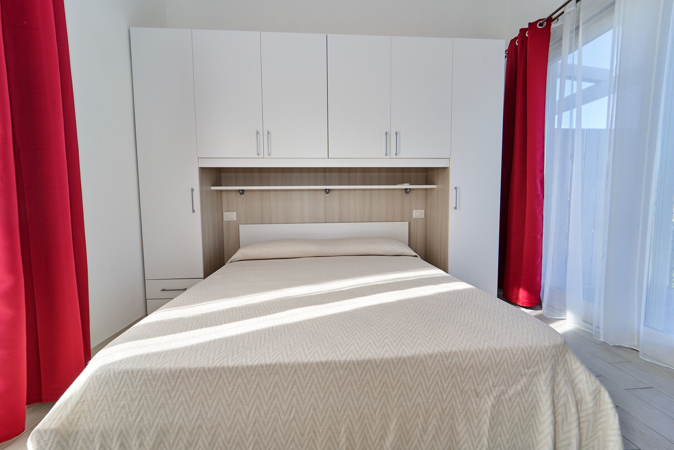 Een slaapkamer met een bed, een witte kast en rode gordijnen.