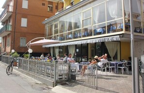 An outdoor seating area with tables and chairs, a bicycle, and a fence. - Hotel Orlov (Rimini)