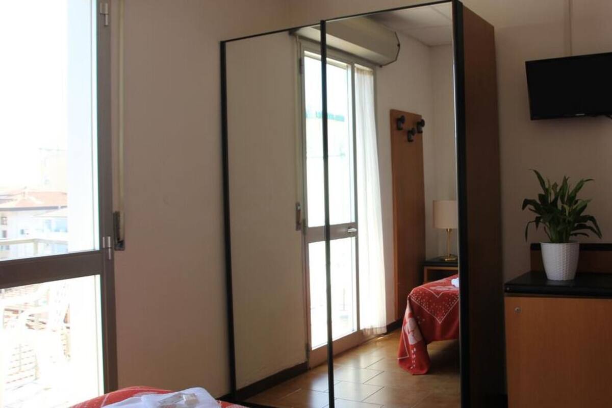 A hotel room with a sliding door, a bed with a red cover, a TV mounted on the wall, and a potted plant on a counter.