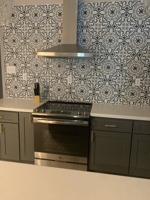 A kitchen with a modern stainless steel stove, dark cabinets, and patterned backsplash tiles.