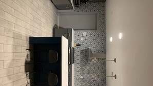 Een moderne keuken met een donkerblauwe kookeiland, twee stoelen, een decoratieve spatwand en een lichtgekleurde betegelde vloer.