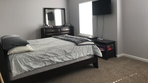 Een slaapkamer met een bed, een dressoir, een televisie en een raam.