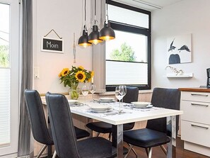 Ein Essbereich mit einem weißen Tisch, gedeckt für vier Personen, schwarzen Stühlen und einer Vase mit Sonnenblumen.