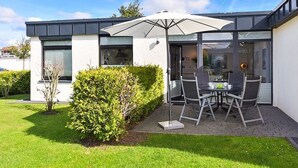 Et moderne hus med en patio, hvor der er et bord og stole under en stor parasol.