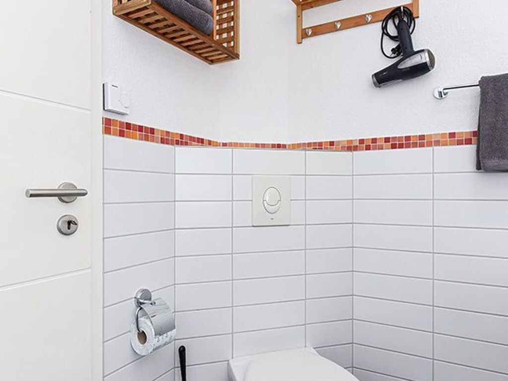 Un baño con paredes de azulejos blancos, ducha en esquina, toallero, secador de pelo y dispensador de papel higiénico.