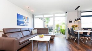 En moderne stue med en brun lædersofa, et hvidt sofabord og et spiseområde med bord og stole.
