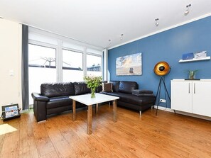 A modern living room with a black leather sofa, a white coffee table, and a blue wall.