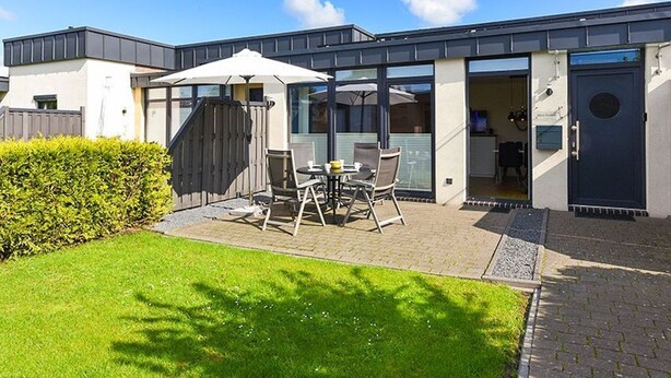 Ein modernes Haus mit Terrasse, einem Essbereich mit Stühlen und Tisch sowie einer überdachten Sitzgelegenheit im Freien.