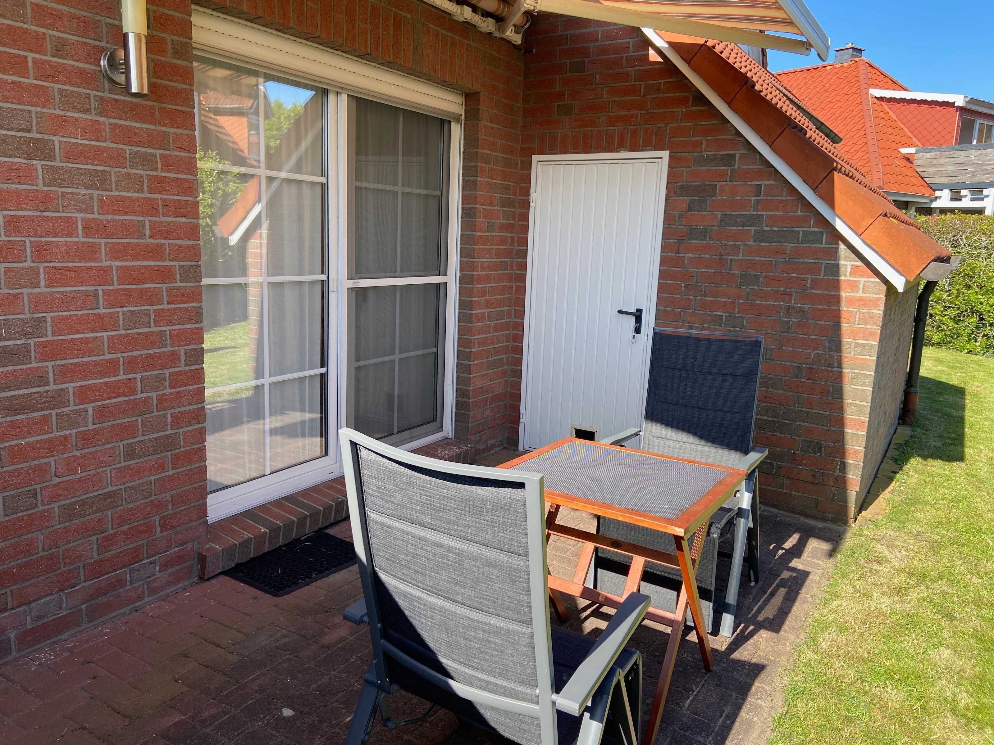 Une terrasse avec une table et des chaises, une porte-fenêtre coulissante et une porte blanche.